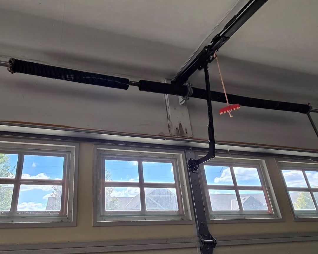 Garage ceiling with black suspended piping above small windows and a red clamp