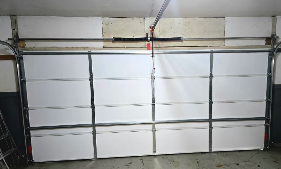 Closed white paneled garage door in a dim garage, with metal tracks and opener hardware above