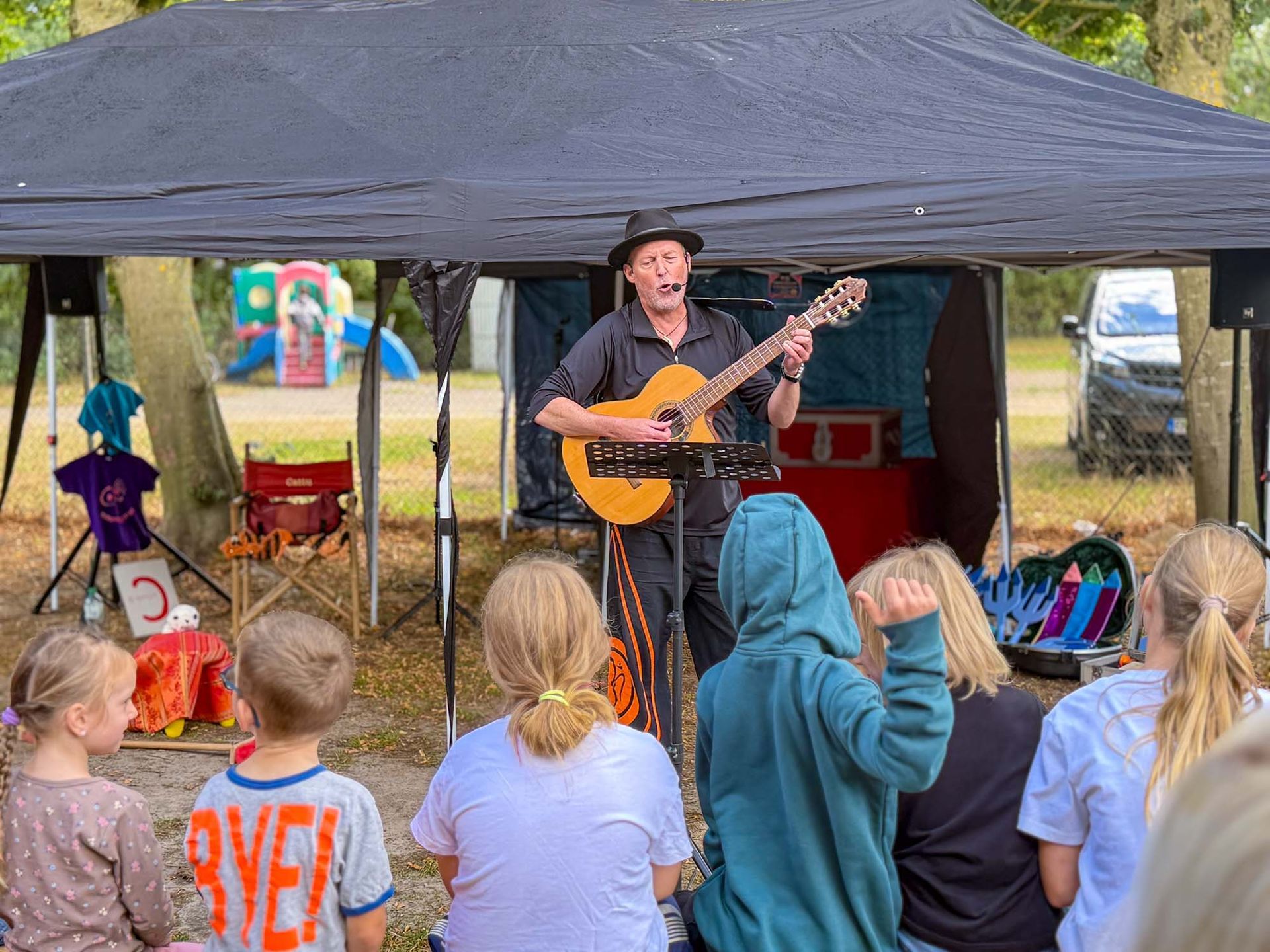 Cattu singt und spielt Gitarre unter einem Zeltdach vor einem sitzenden Publikum im Freien