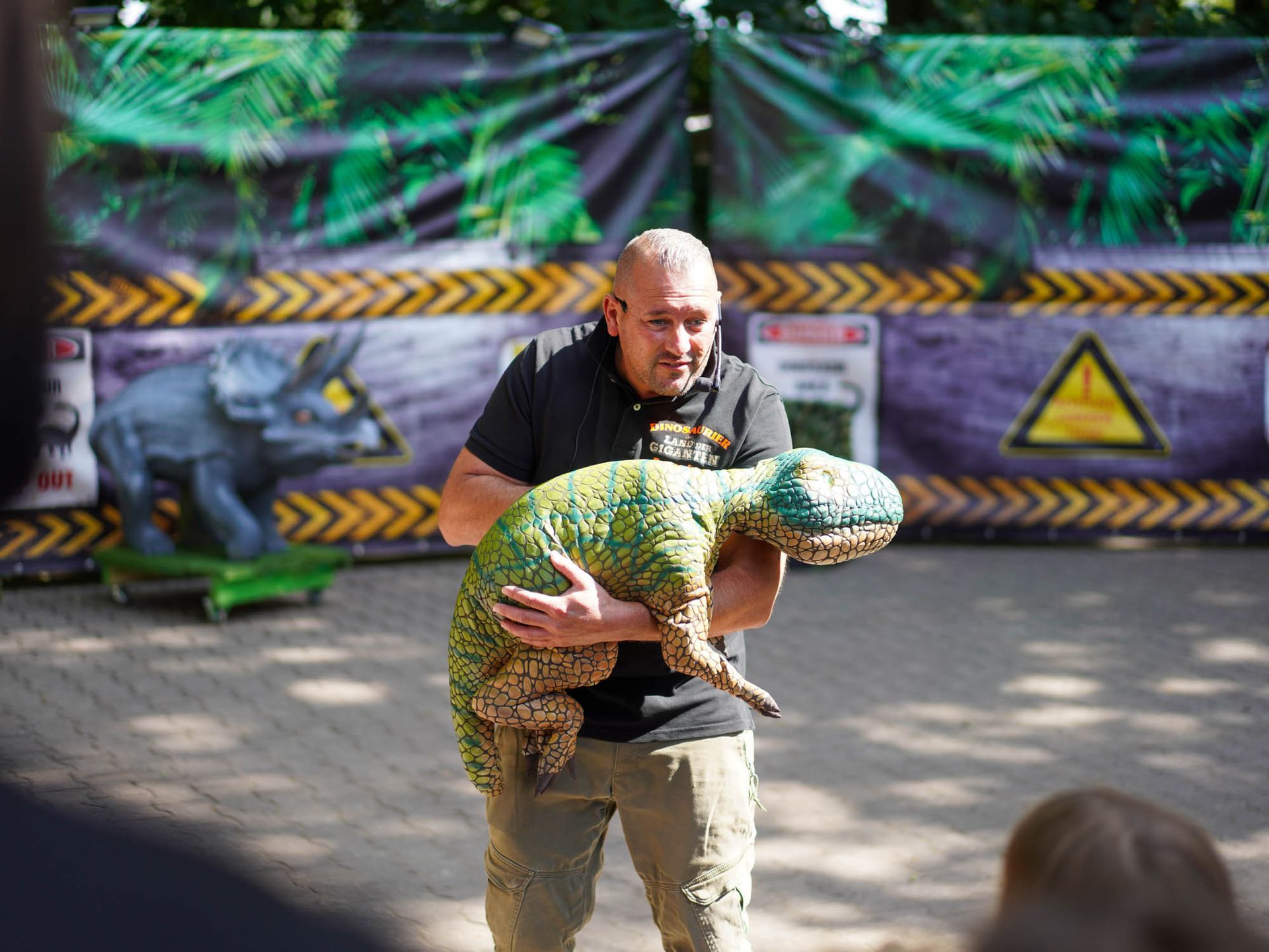 Mann hält eine kleine, realistische Dinosaurierpuppe bei einer Veranstaltung zum Thema Dinosaurier. 