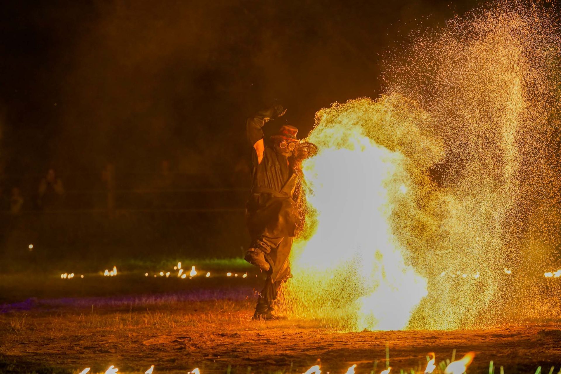 Person neben einem großen Feuerball bei Nacht, Funken fliegen vor dunklem Hintergrund