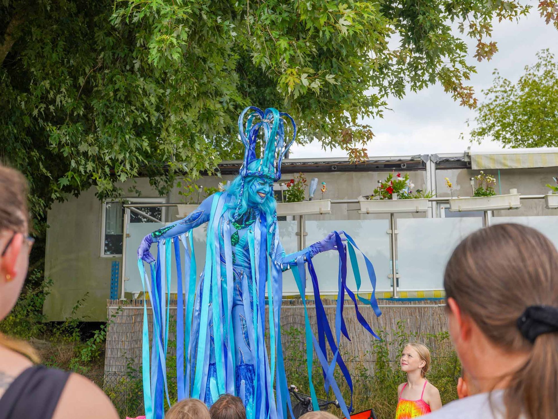 Eine in Blau verkleidete Frau in einem Innenhof, während Menschen im Vordergrund zu sehen sind.