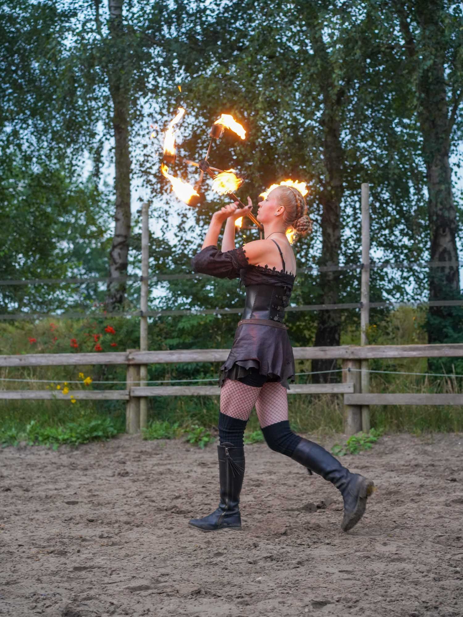 Eine Person in schwarzer Kleidung führt bei Dämmerung im Freien einen Feuertanz auf.
