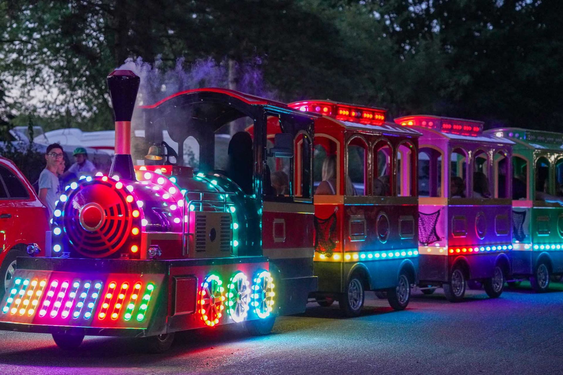Bunt beleuchtete Bimmelbahn bei Dämmerung, mit Neonlichtern, die an der Lokomotive und den Waggons leuchten.