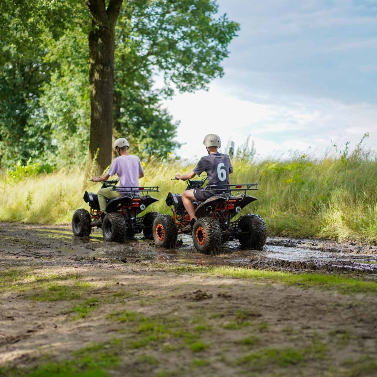 Zwei Kinder fahren mit einem Quad auf einem schlammigen Pfad unterwegs