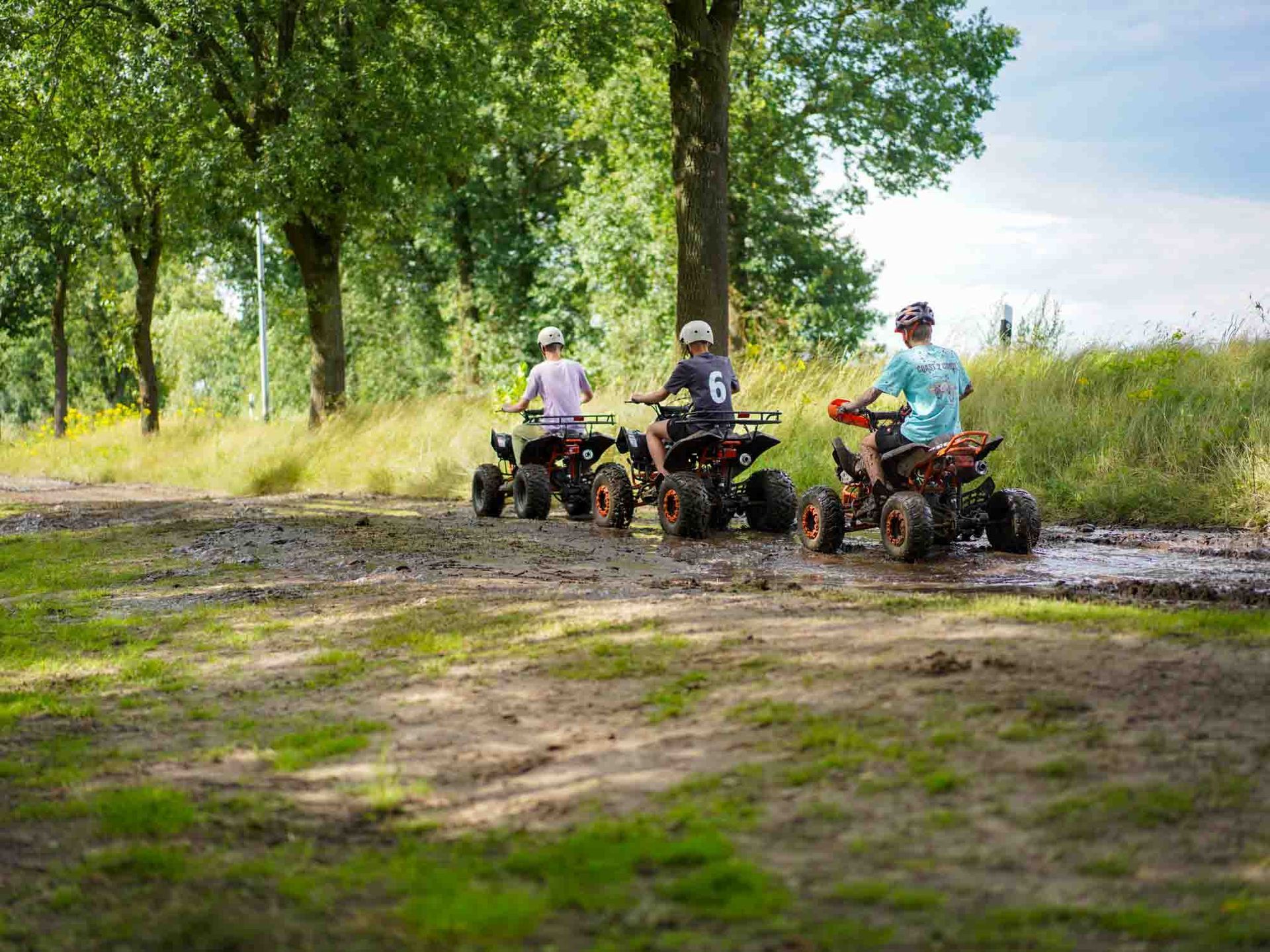 Drei Kinder fahren mit einem Quad auf einem schlammigen Pfad