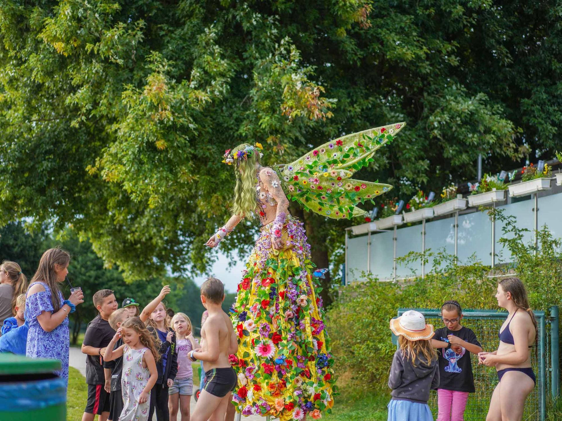Eine Blumenfee umgeben von Kindern, die ihre Hände ausstrecken.