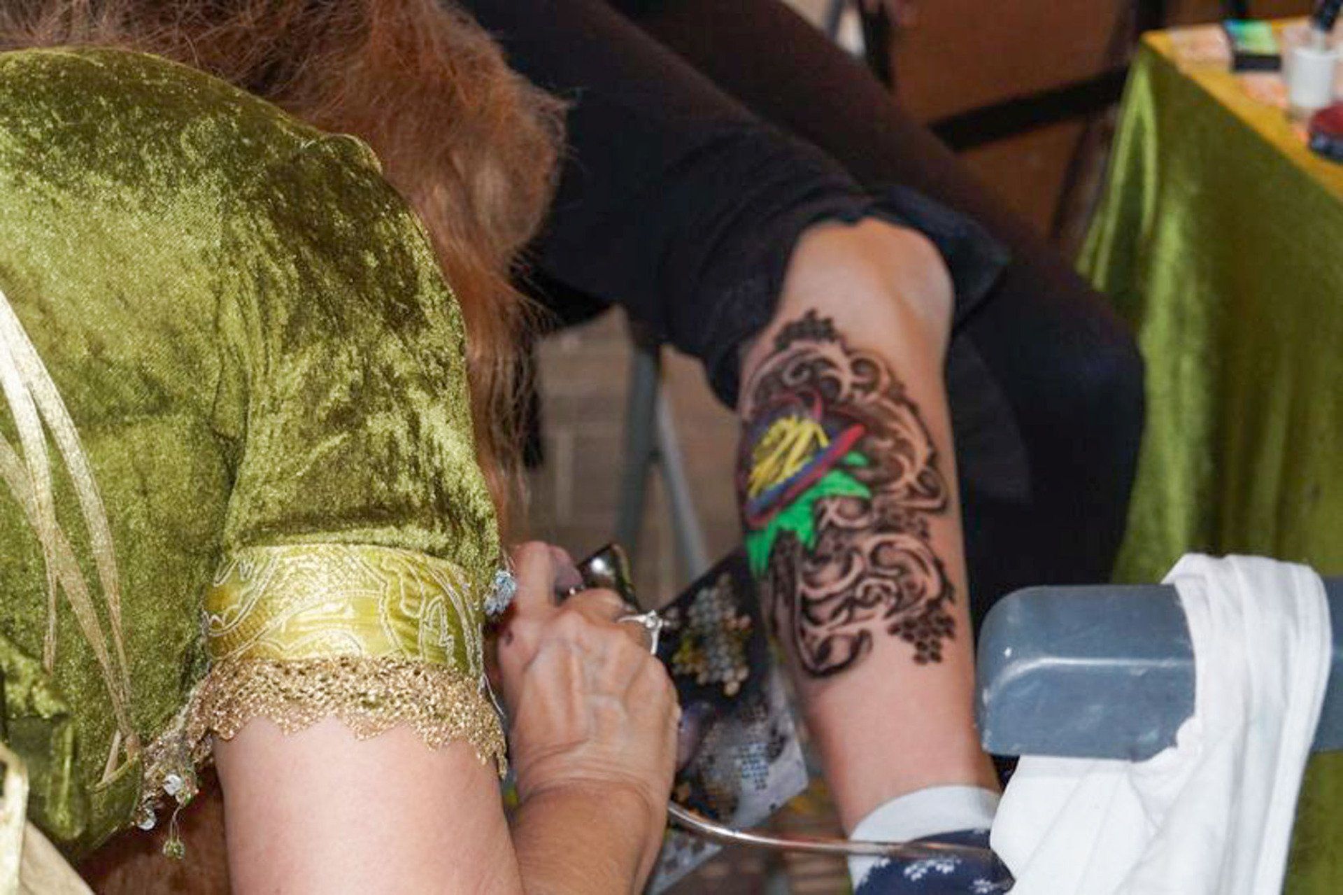 Person, die kompliziertes Design mit grüner und brauner Farbe auf den Arm airbrusht.
