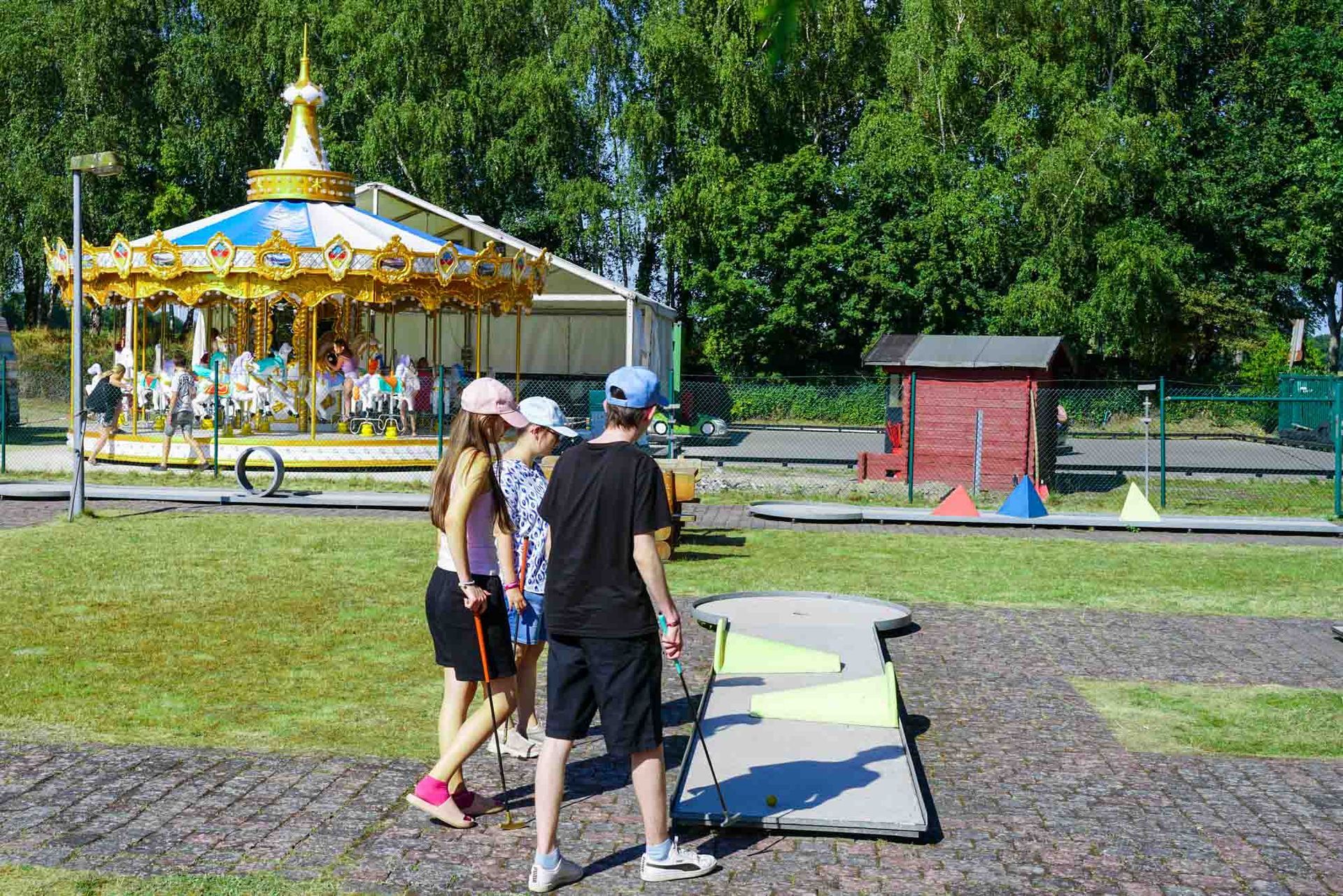 Zwei Menschen gehen auf einem Parkweg an einem Karussell und einem kleinen roten Kiosk vorbei.