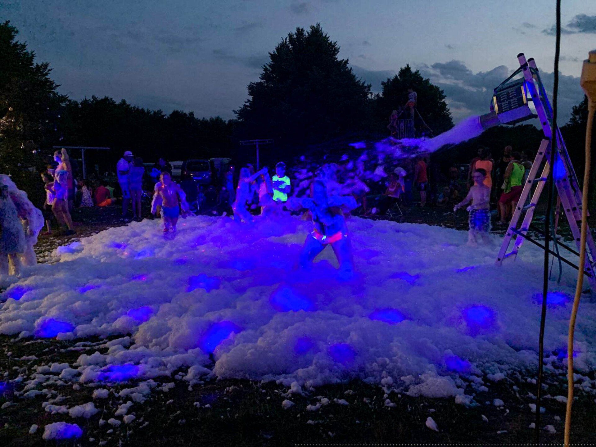 Menschen stehen nachts in einer Schaumgrube, die von blauen Lichtern beleuchtet wird