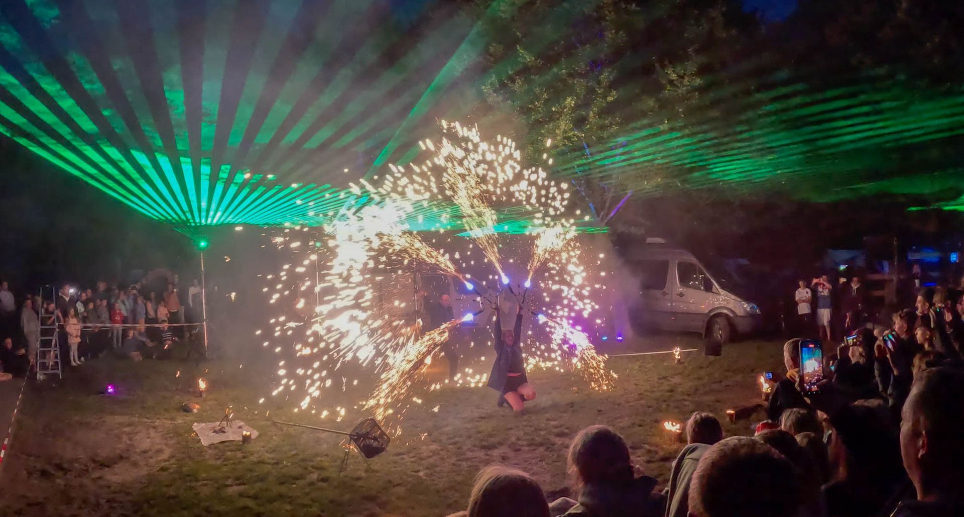 Feuertänzer tritt mit Funken und grünen Lasern bei einer Veranstaltung im Freien auf.