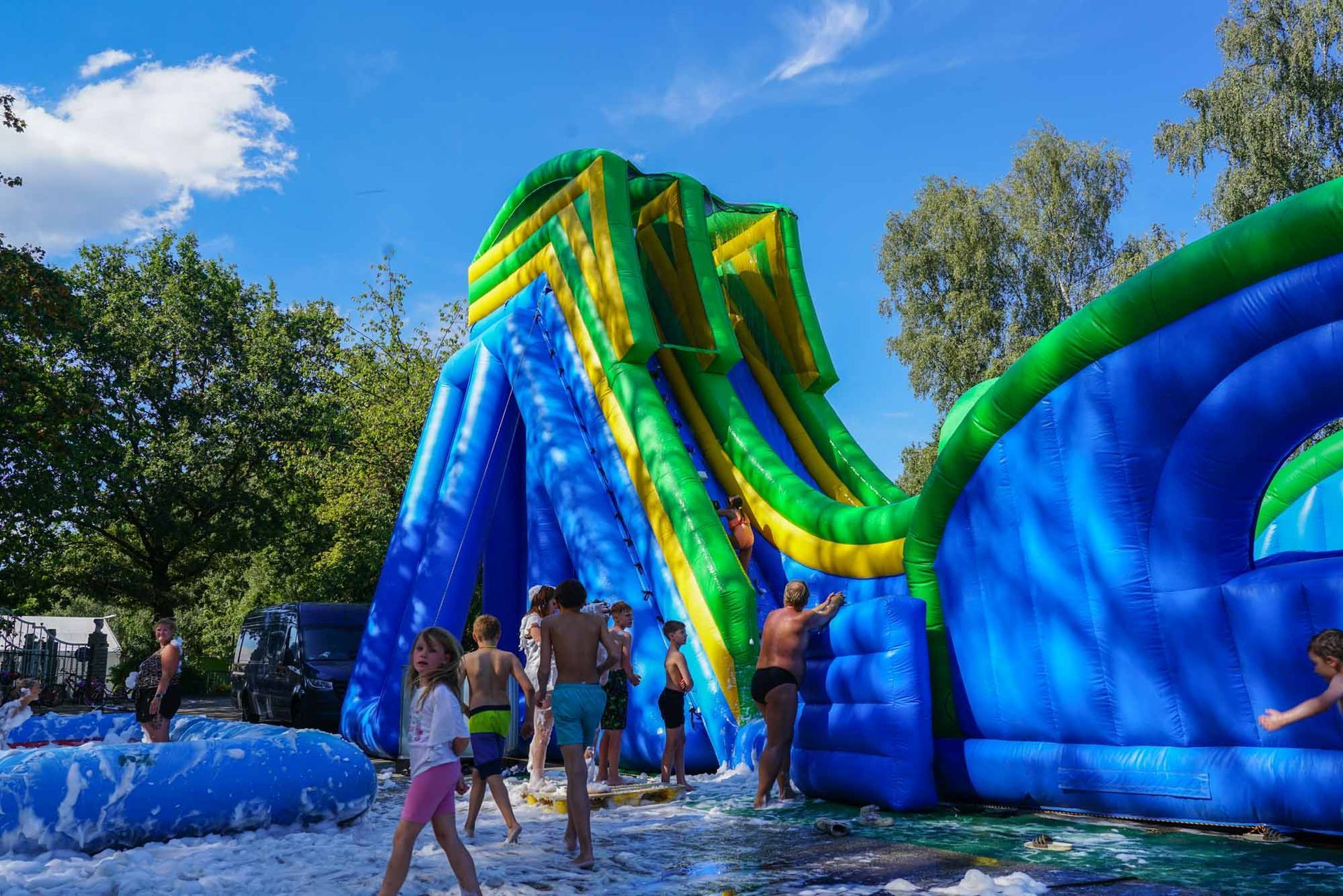 Menschen, die auf einer blau-grünen aufblasbaren Hüpfburg, funktional als Wasserrutsche, klettern