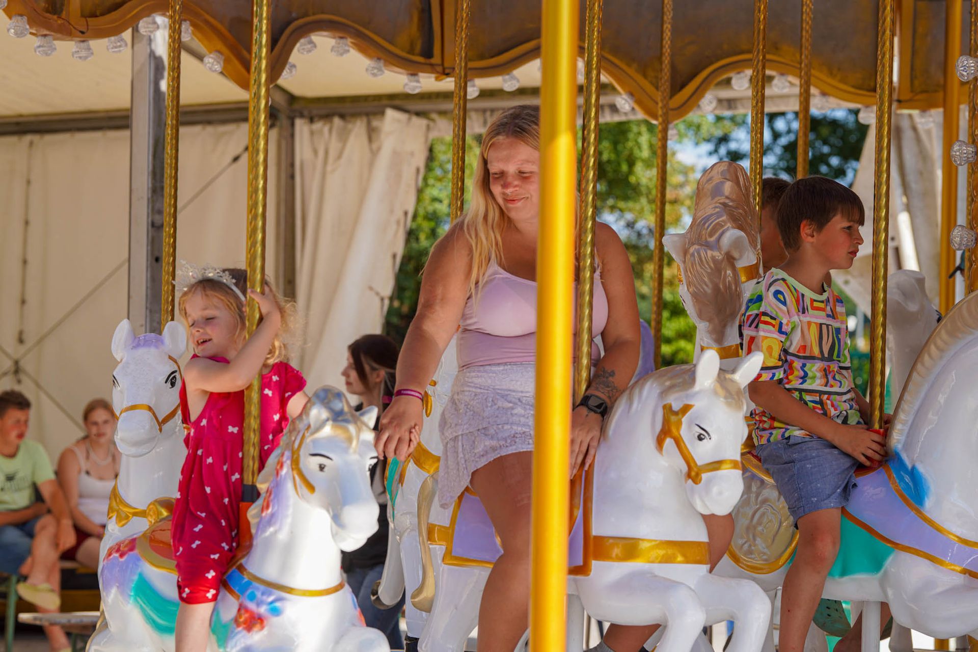 Zwei Kinder und eine Frau auf weißen Karussellpferden