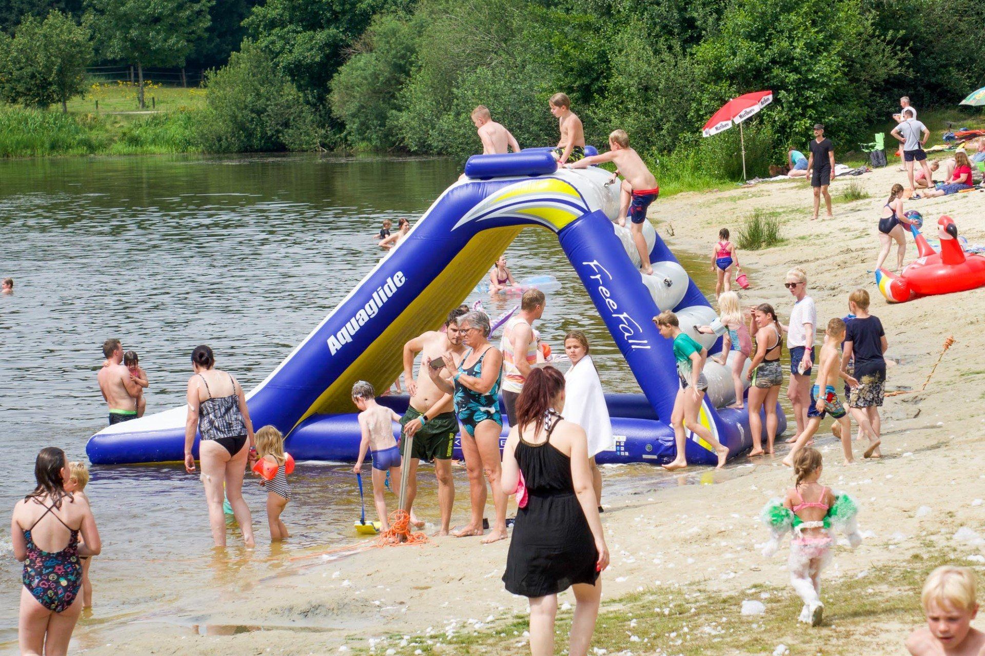 Menschen an einem See mit einer blauen aufblasbaren Wasserrutsche