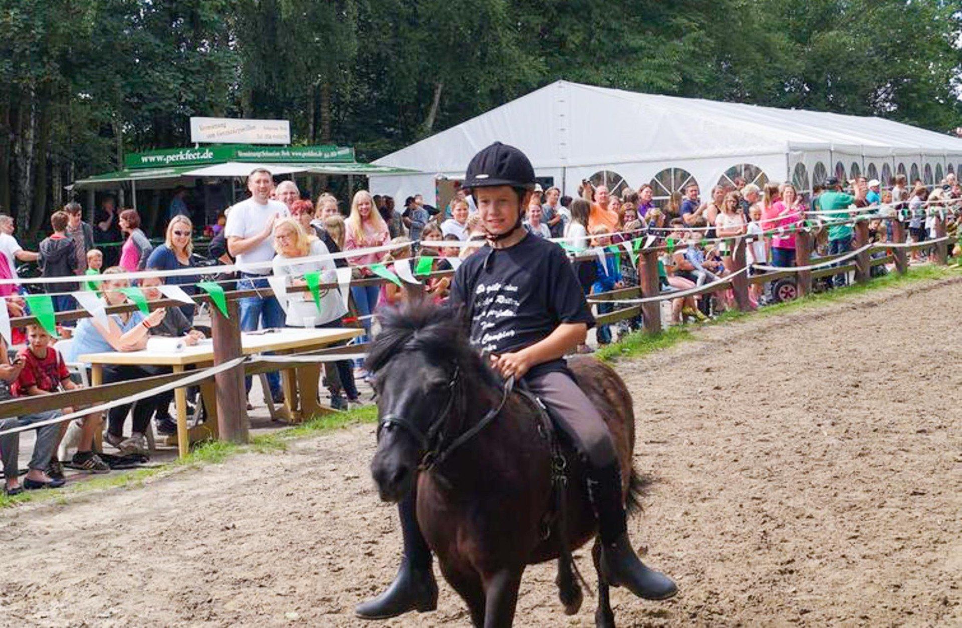 Junge auf einem dunklen Pony reitet. Zuschauer beobachten die Veranstaltung
