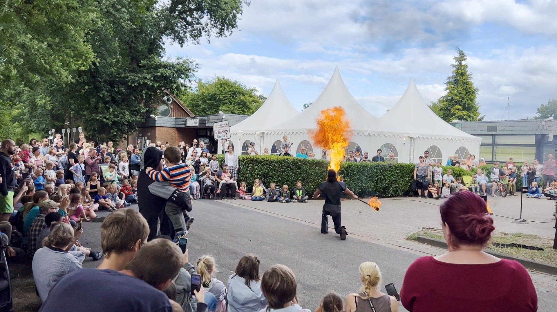 Ein Künstler speit Feuer vor einer Menschenmenge und weißen Zelten