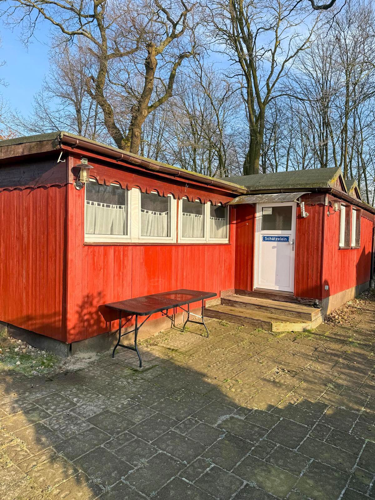 Rotes Holzgebäude mit weiß gerahmten Fenstern und einer weißen Tür; davor eine Bank im Freien.