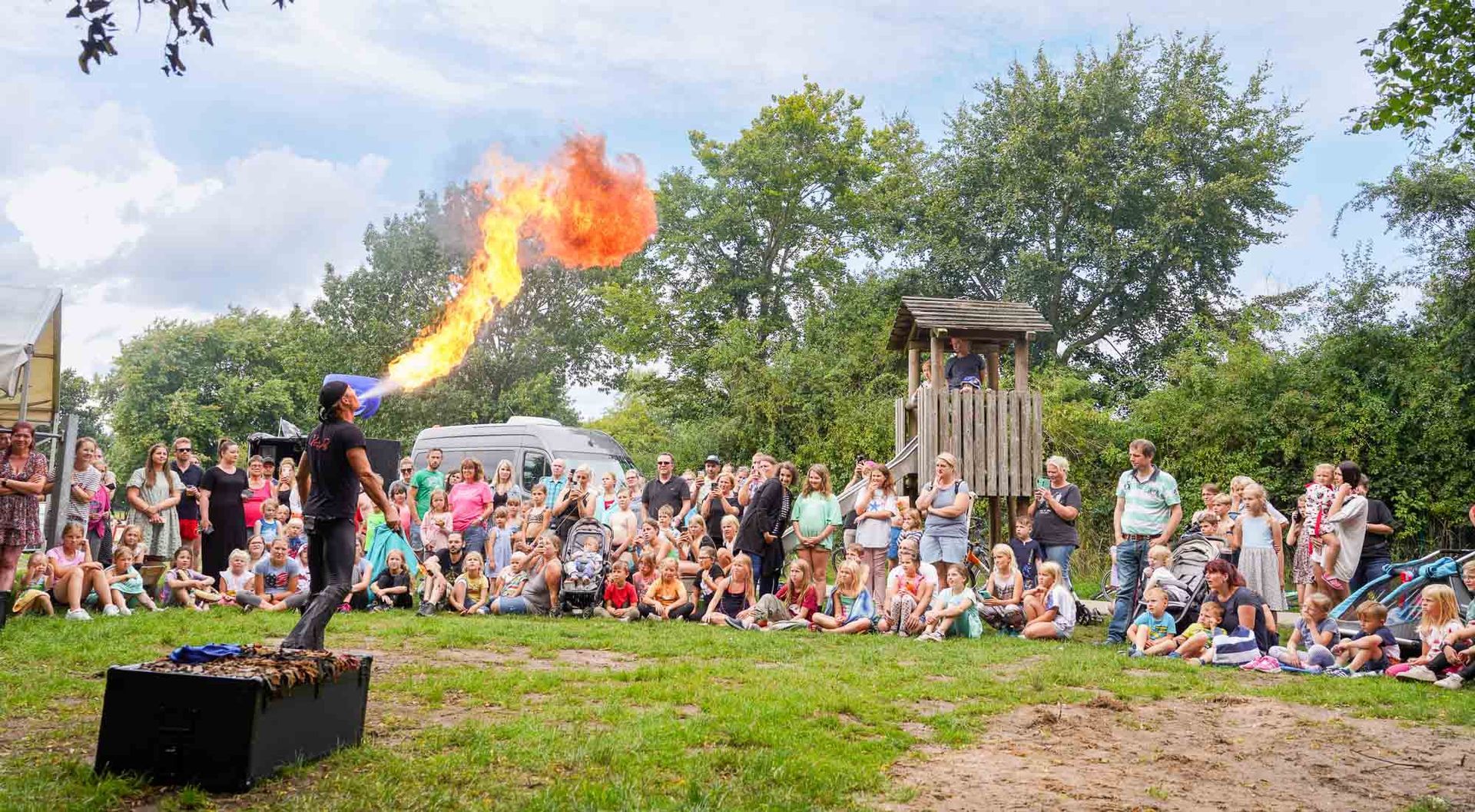 Feuerspucker tritt vor einer Menschenmenge auf einer Wiese auf. 