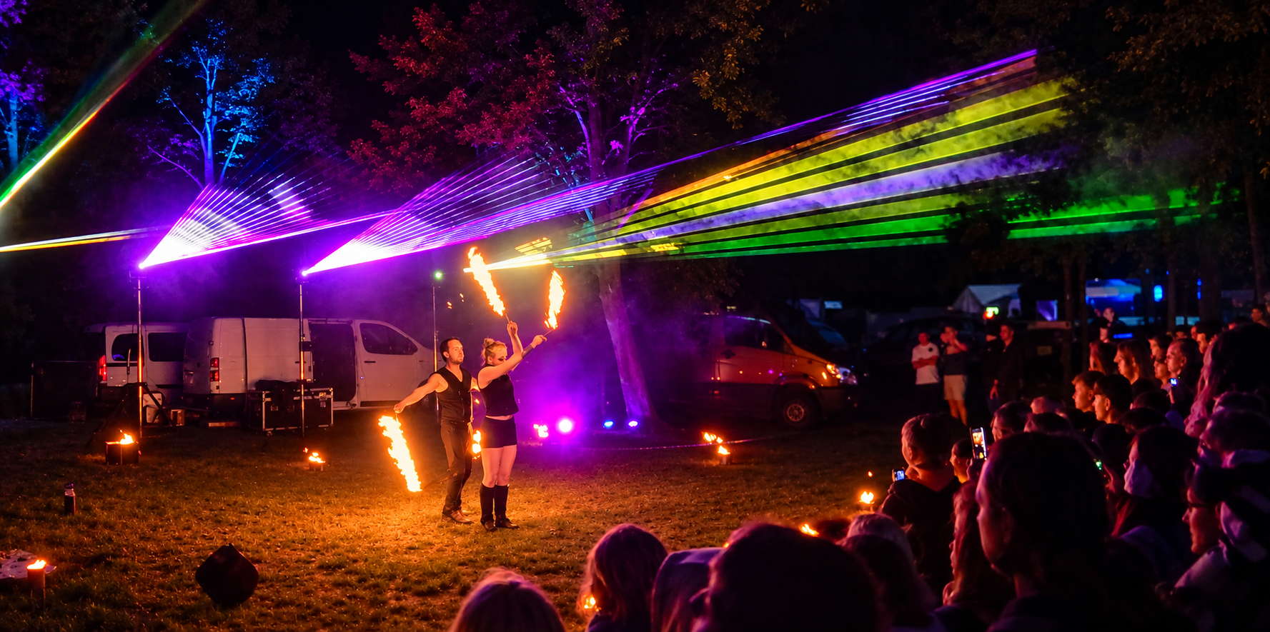 Nächtliche Lasershow im Freien mit leuchtend violetten, grünen und gelben Strahlen über einer Menschenmenge