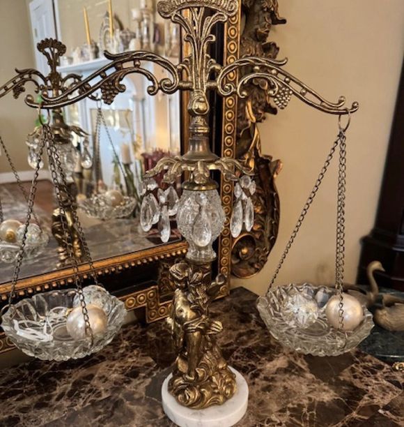 Ornate gold-and-silver tabletop scale with crystal bowls and candle holders on a marble surface near a mirror