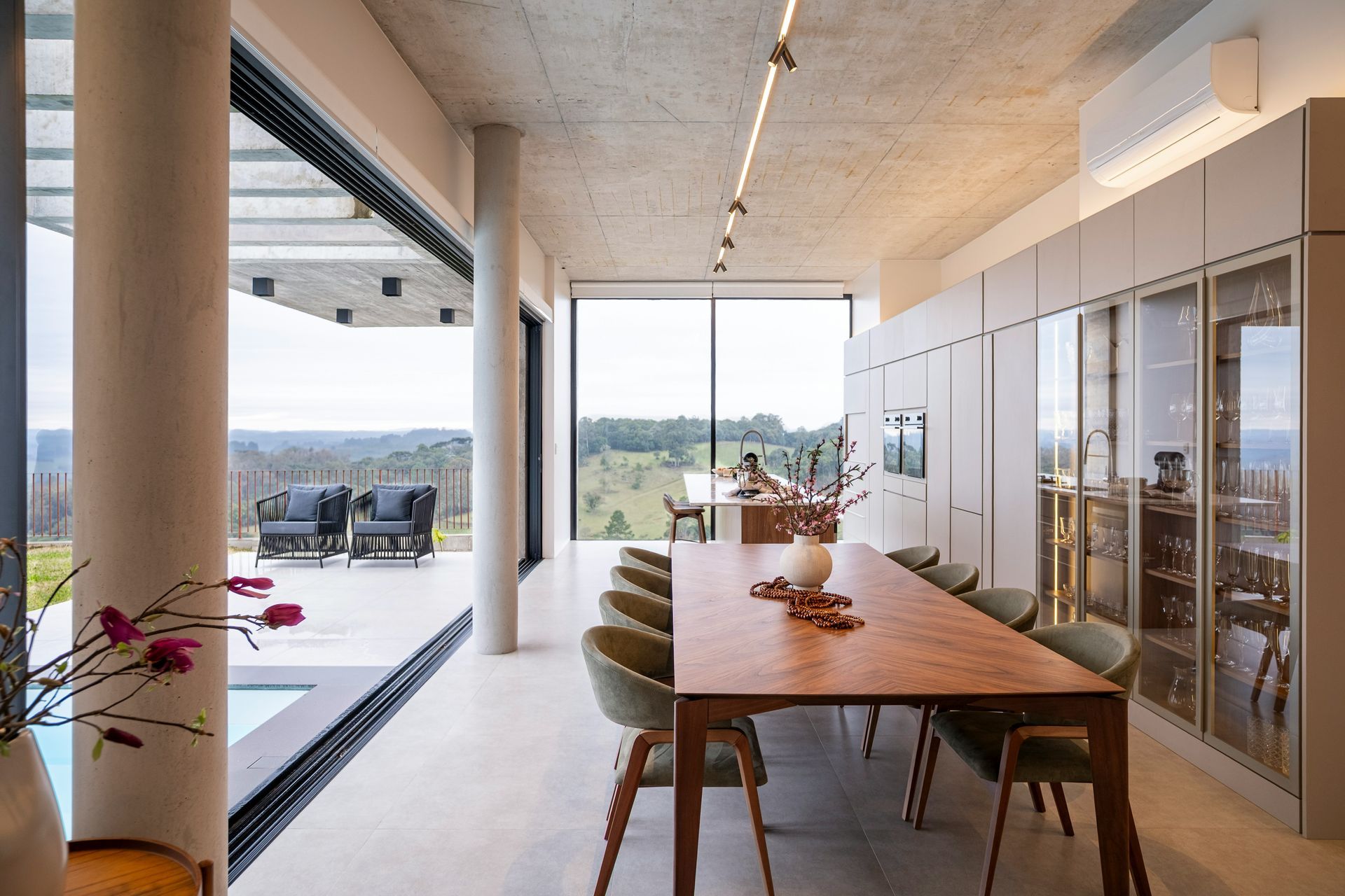 Modern dining room with wooden table, glass cabinets, and open view to a patio and landscape.