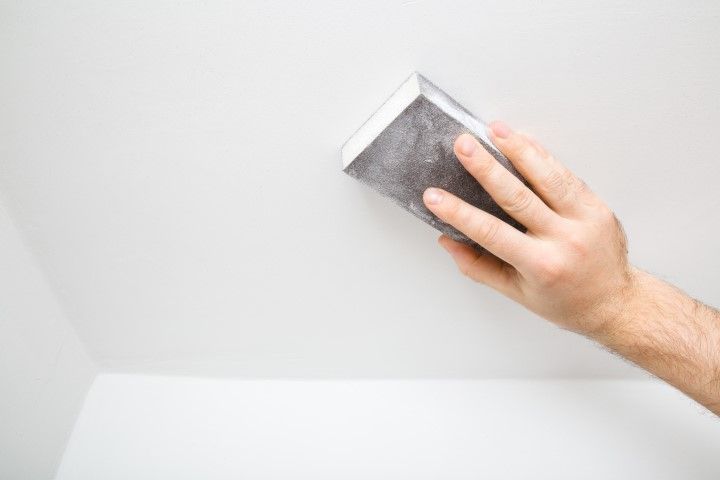 Hand sanding a white painted surface with a sanding block.