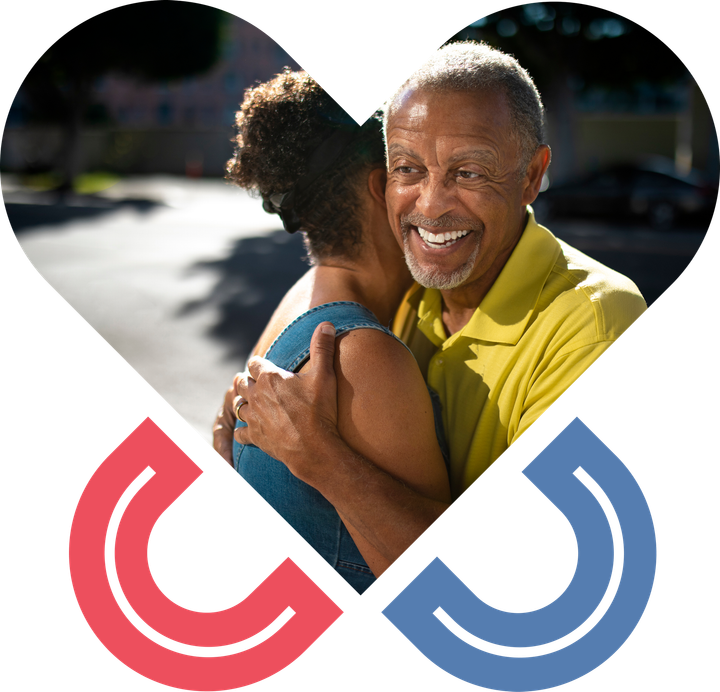 Smiling man in a yellow shirt hugging someone, with red and blue heart-shaped logos below.