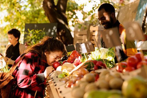 A woman smells an apple at a farmers market stall.