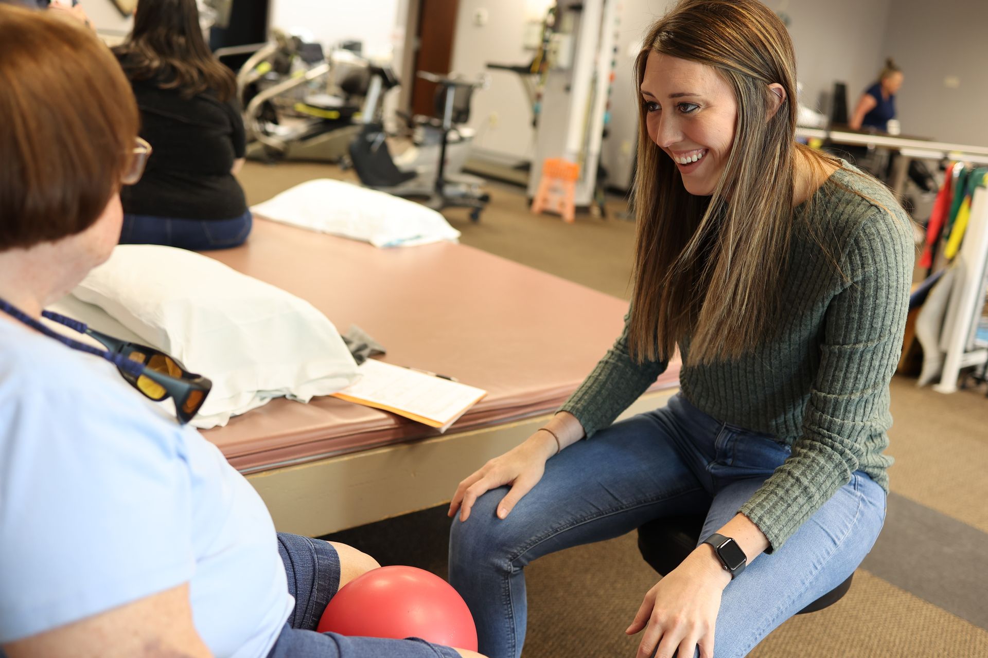 Two people talking in a classroom, one seated on a desk and smiling while the other listens.