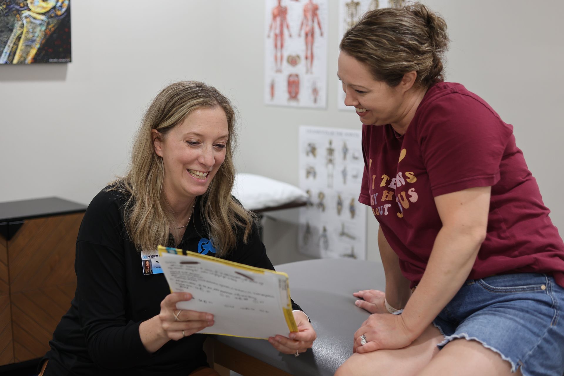 Two women smiling and reviewing paperwork in a clinic exam room