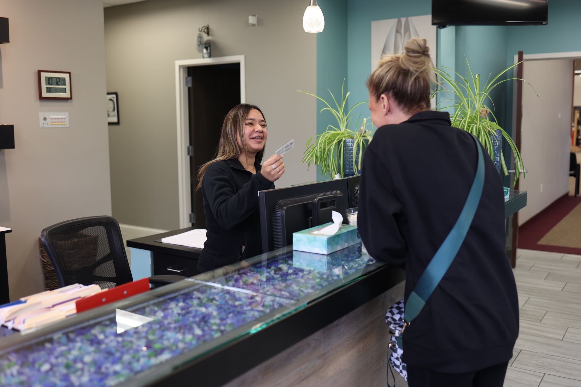 Woman at a reception desk smiling and talking with a visitor in a lobby.