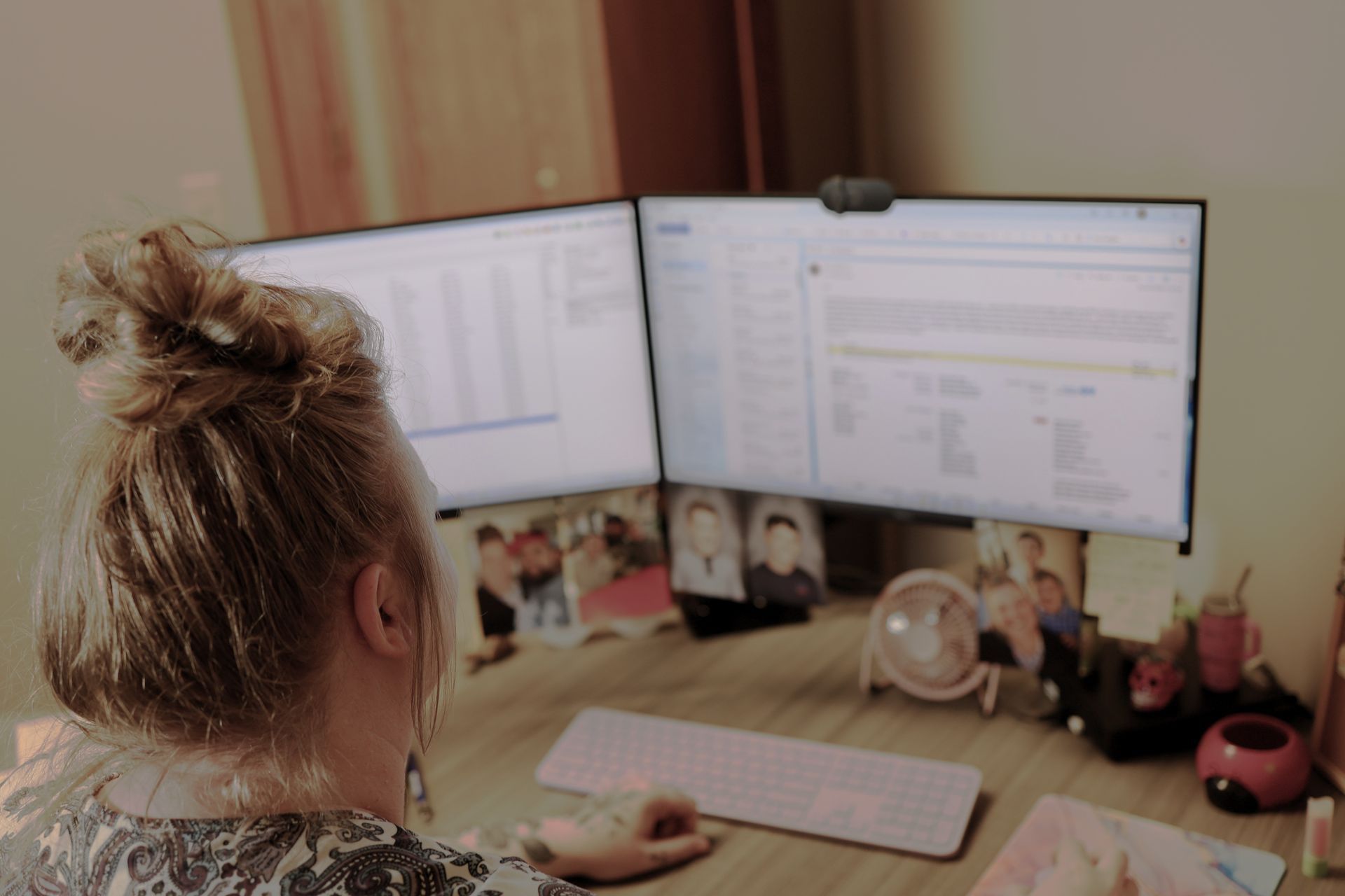 Person working at a desk with dual monitors in a home office, using a keyboard and mouse.