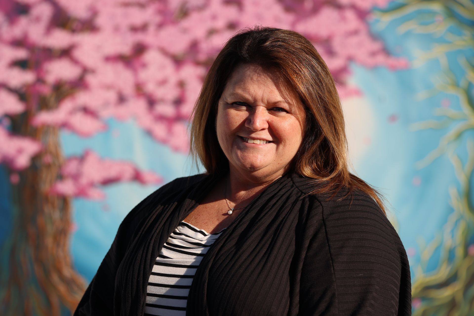 Smiling woman in a black cardigan against a colorful pink and blue mural backdrop