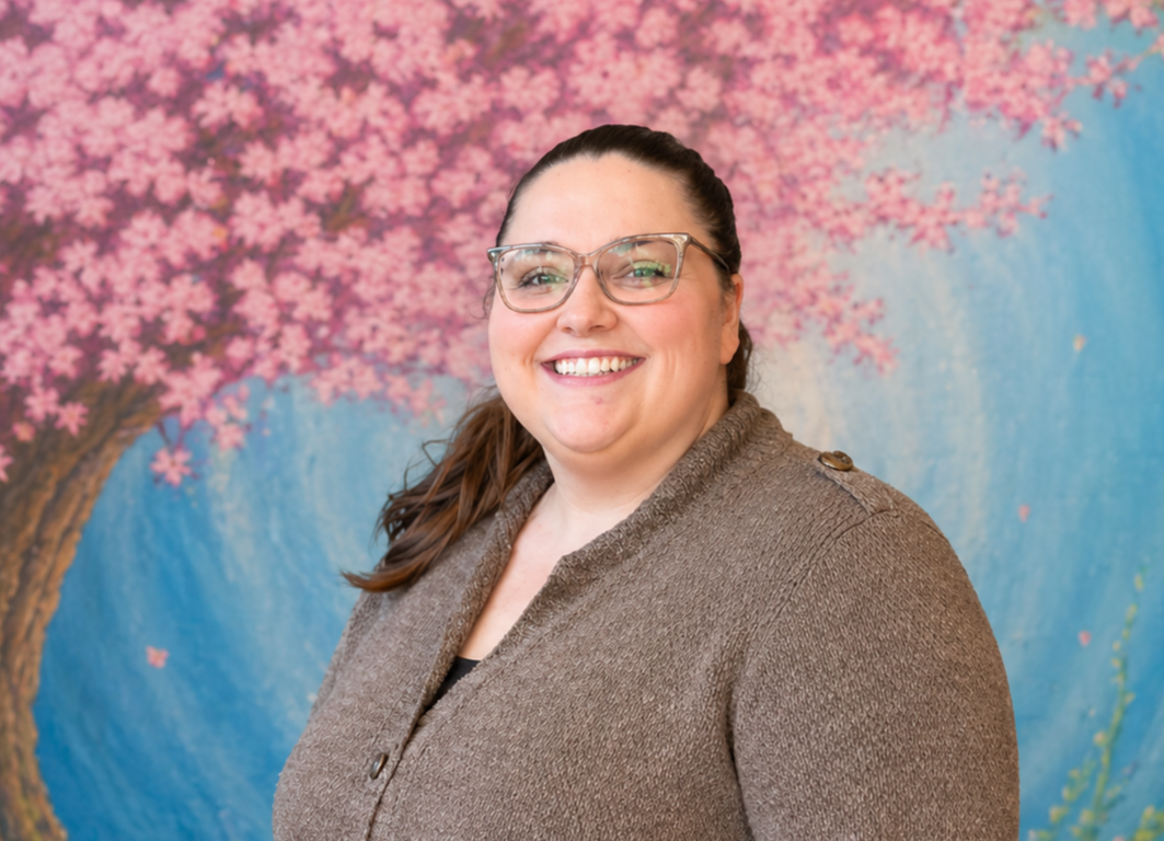 Smiling person in glasses and brown sweater against a blue and pink floral backdrop
