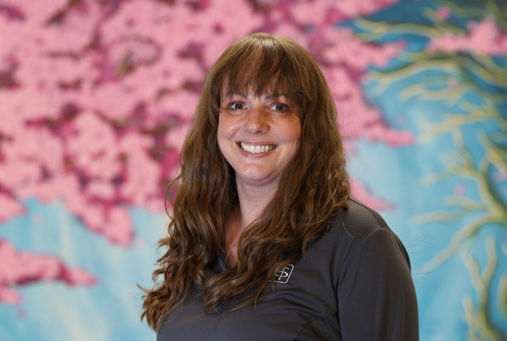 Smiling person in a dark shirt standing before a pink and blue floral mural.