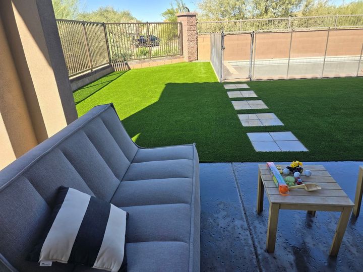 Patio with gray sofa, small wooden table, and green lawn with stepping stones in a sunny backyard