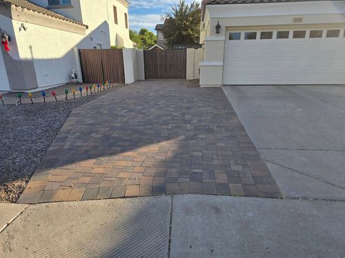 Residential driveway with paver extension and a white garage door, bordered by gravel and a wooden fence.