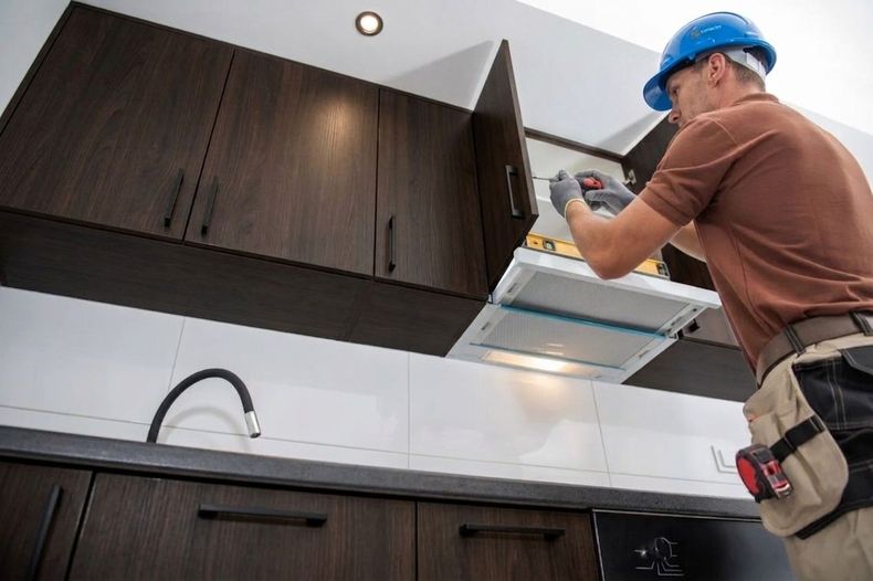 Technician in blue hard hat installing a cabinet light in a modern kitchen