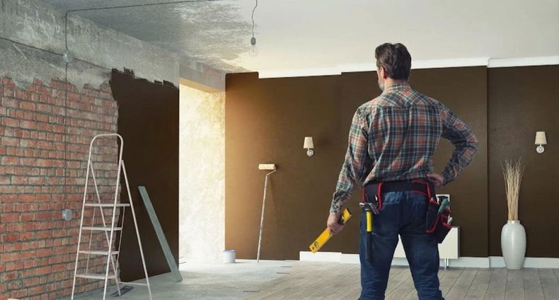 Person in plaid shirt working in a partially renovated room with brick wall and painting tools