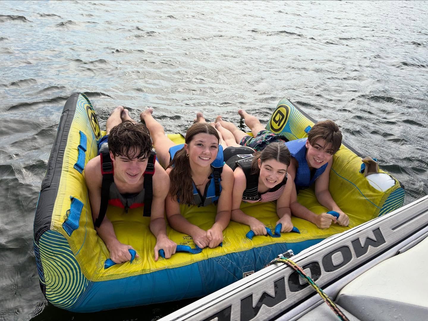 Four friends smiling on a yellow-and-blue inflatable raft in the water