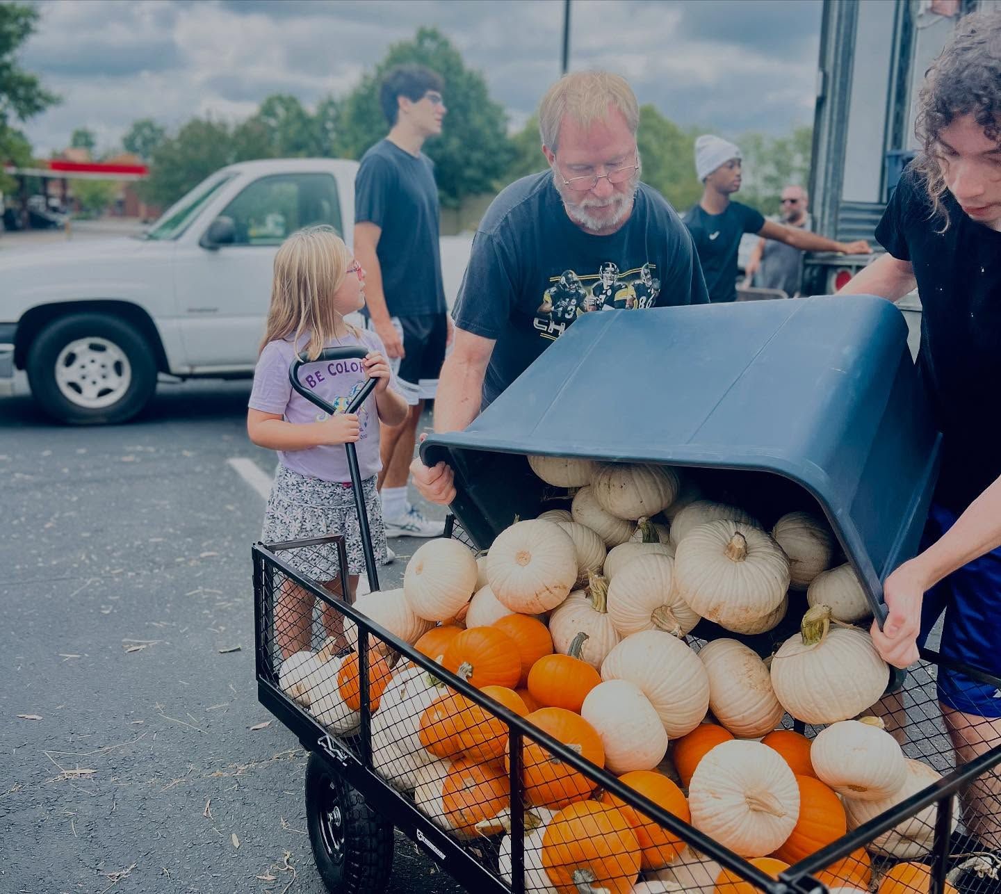 People loading white and orange pumpkins from a cart at an outdoor market
