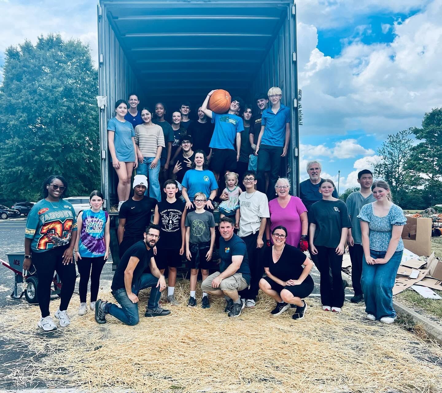 Group of people posing in front of a large truck on a gravel road under a bright sky.
