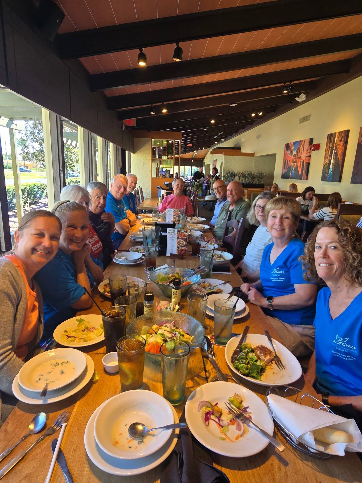 People seated at a long restaurant table, smiling and enjoying a meal together.