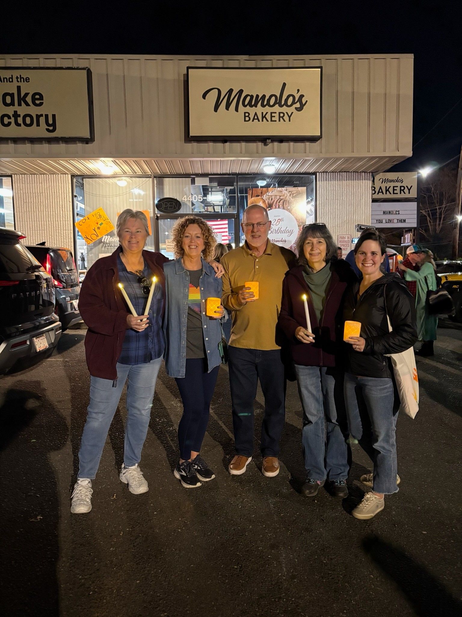 Six people smiling outside Momo’s Bakery at night, standing together in front of the lit storefront.