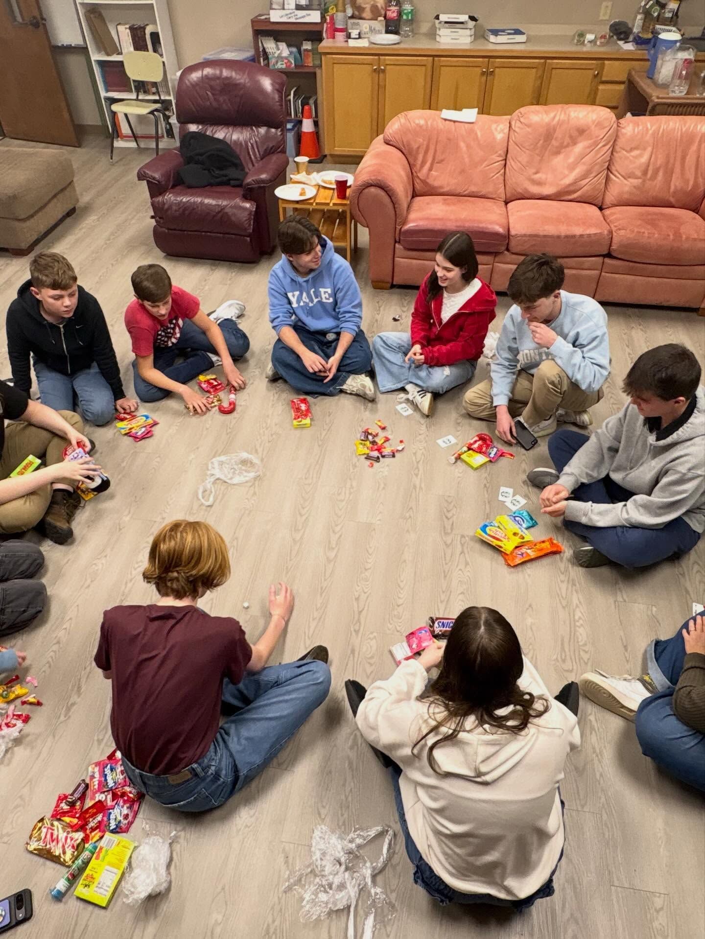 Children sitting in a circle on a classroom floor, opening colorful snack or craft bags together