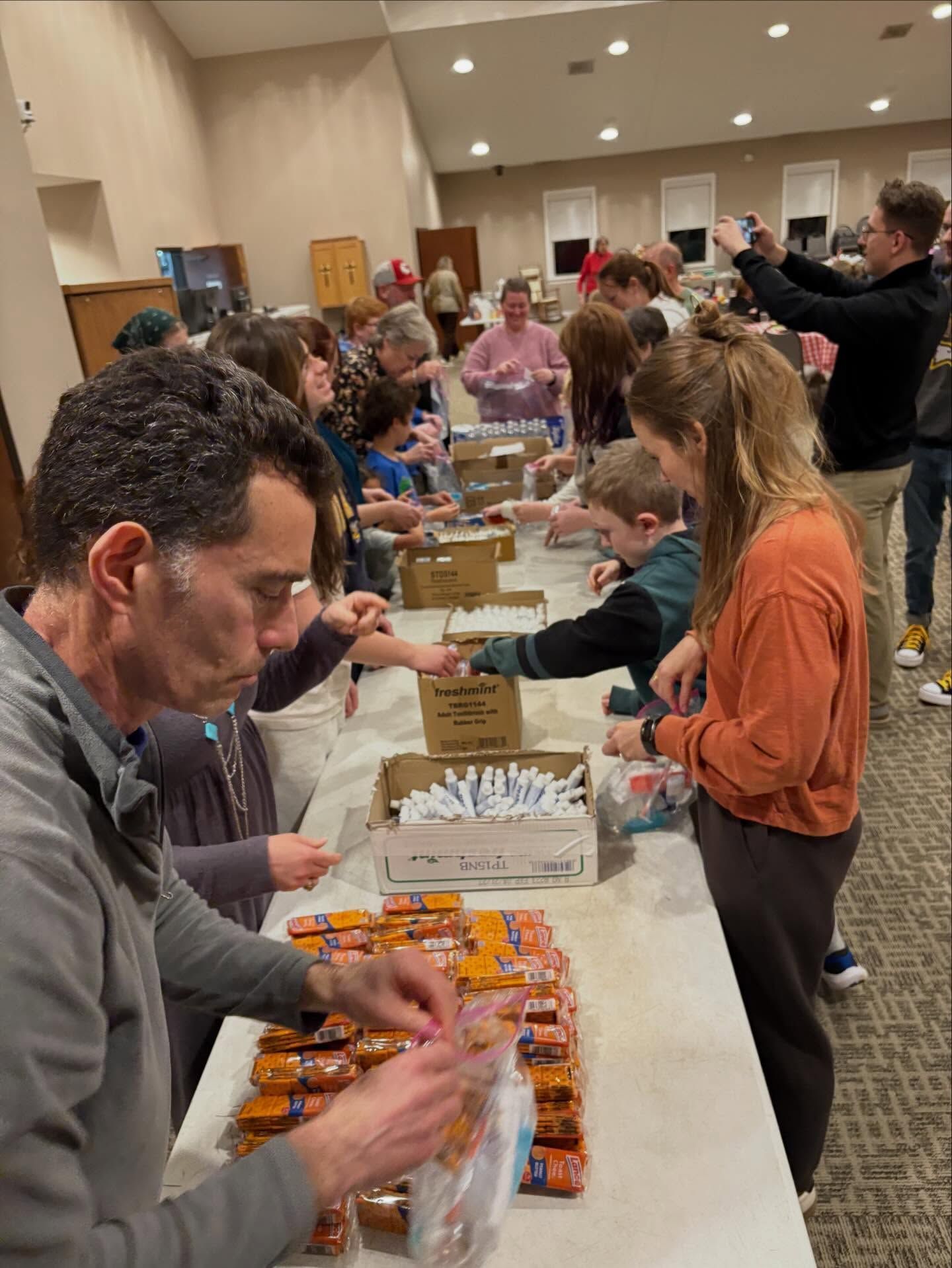 People serving drinks and snacks at a crowded indoor table in a banquet hall