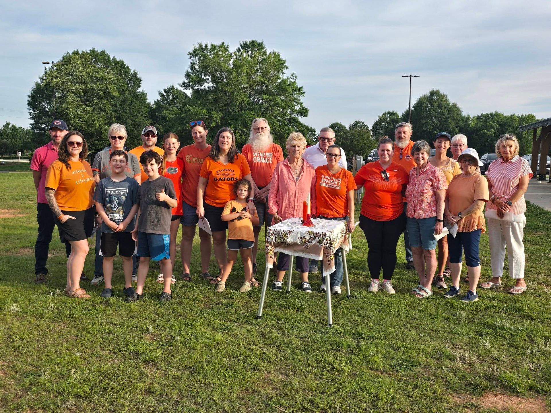 Group of runners posing outdoors in bright orange shirts beside a small table on a grassy field