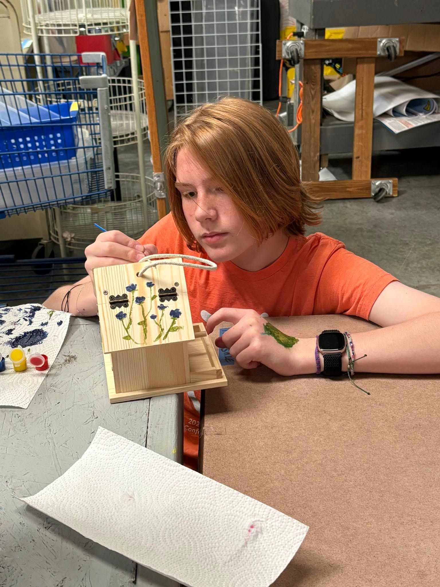 Person in an orange shirt examining a small handmade craft at a table in a workshop-like room