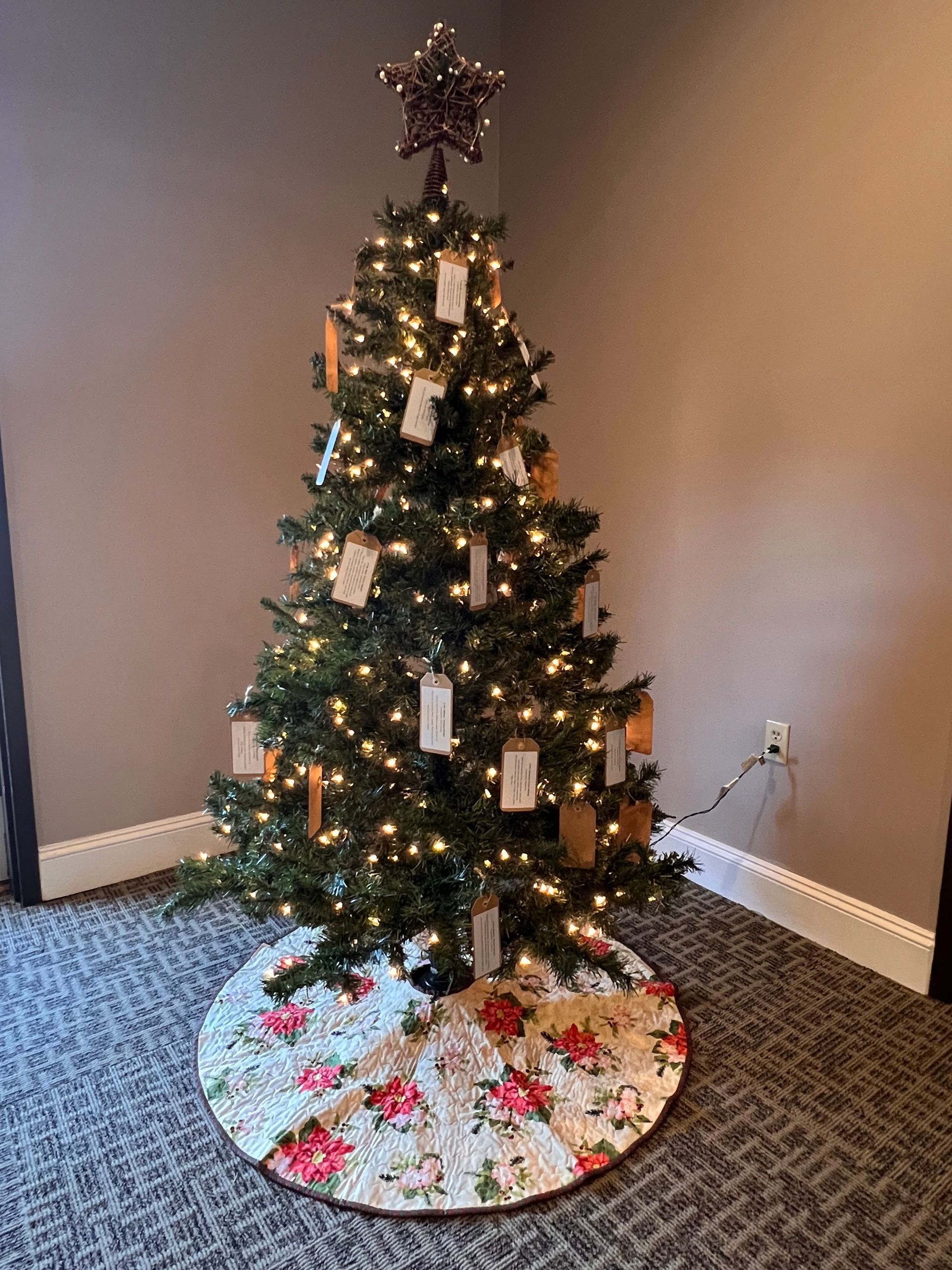 Decorated Christmas tree with lights and ornaments on a floral skirt in a carpeted corner