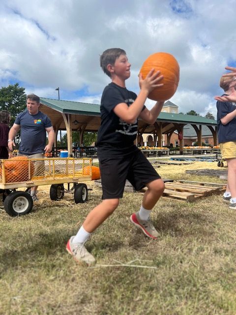 Teen in black sportswear catches an orange basketball outdoors on a grassy field.